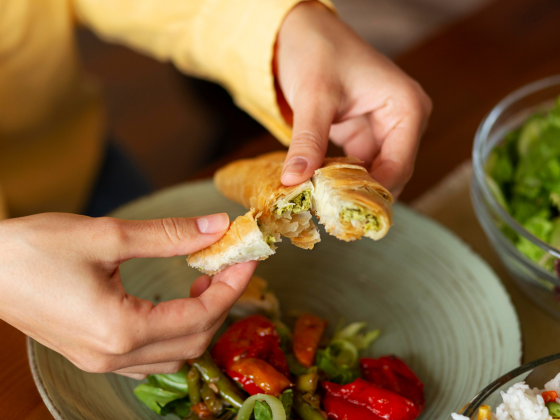 Joven cortando un croissant en la cocina con vegetales de fondo, simbolizando la alimentación flexible y saludable en L'Hospitalet de Llobregat.