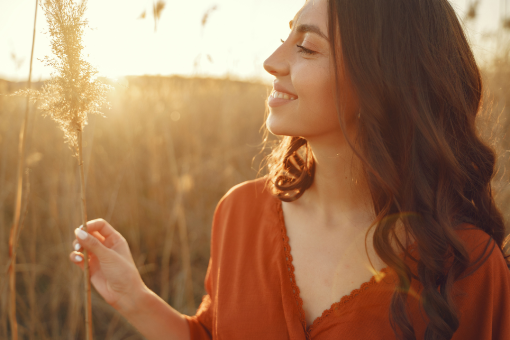 Mujer feliz disfrutando de una puesta de sol en un campo, simbolizando el bienestar mental alcanzado a través de una buena nutrición.